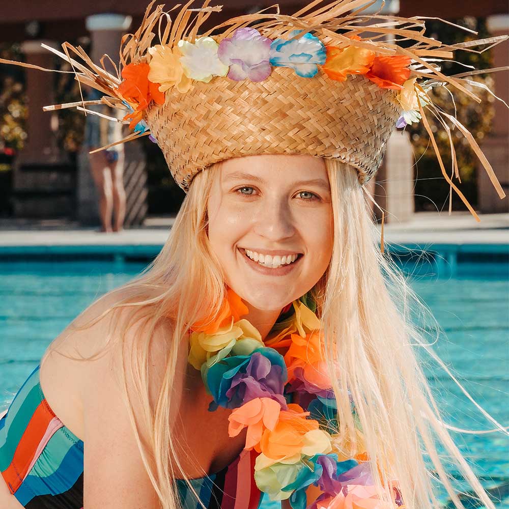 woman wearing hawaiian outfit and hawaiiian hat smiling having fun at pool party