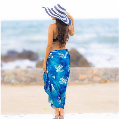women in blue beach wrap with turtle print posing with hat